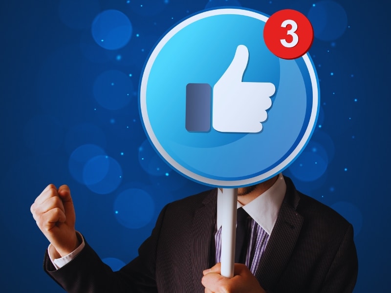 Man in suit holding Facebook like icon sign with notifications, symbolising success as a Facebook marketing partner.